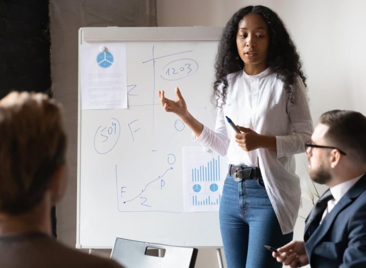 African American Businesswoman Giving Flip Chart Presentation At Briefing African American businesswoman giving flip chart presentation at briefing, female coach mentor explaining project strategy, plan, explaining diagrams, employee presenting financial report with stats